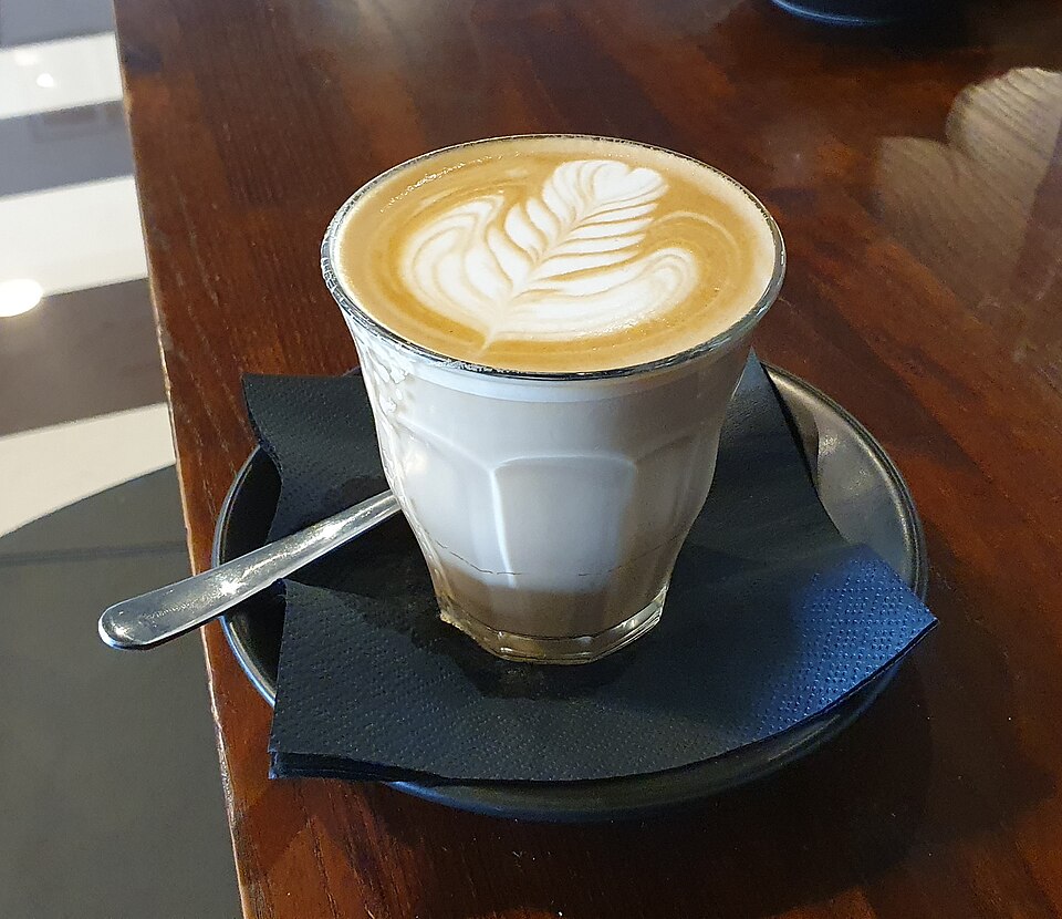 A latte with rosetta latte art in a glass on a cafe table